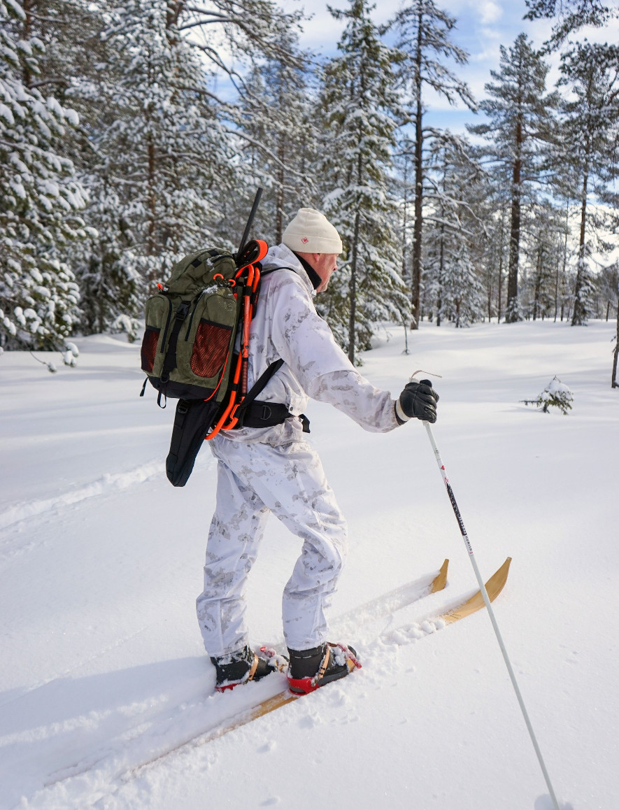 Jägare med vapen på ryggen, ståendes på Olskogens jaktskidor i trä